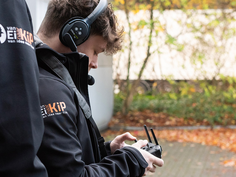 Cameraman en dronepiloot met een DJI Mavic dronecontroller op een filmset, gericht op het vastleggen van luchtbeelden voor een bedrijfsfilm, combineert vaardigheden in filmmaken en dronebesturing voor professionele bedrijfsvideo's.