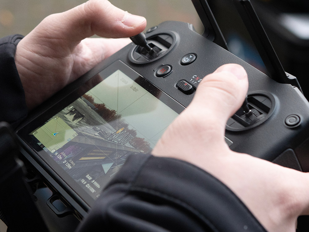 Cameraman en dronepiloot bedient een DJI Mavic dronecontroller op een filmset, gespecialiseerd in het maken van luchtbeelden voor bedrijfsfilms en bedrijfsvideo's, een essentieel onderdeel van moderne filmmaking.