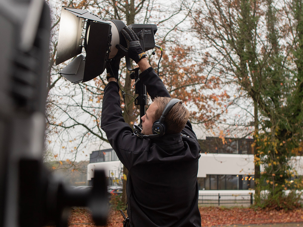 Een gaffer in Veenendaal werkt aan de belichting op een filmset met een spot en diverse filmlichten, samen met een filmmaker en de rest van de filmcrew om de scène perfect uit te lichten